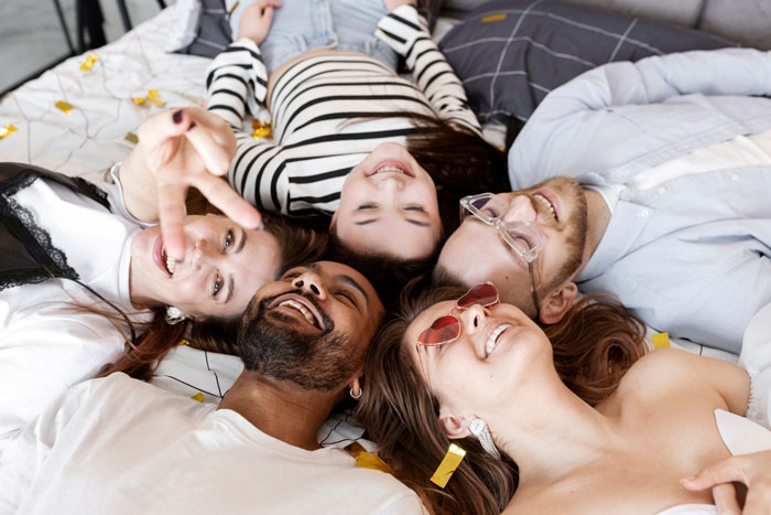 Group of friends lying on bed, smiling and enjoying time together, reflecting relationship and trust dynamics.