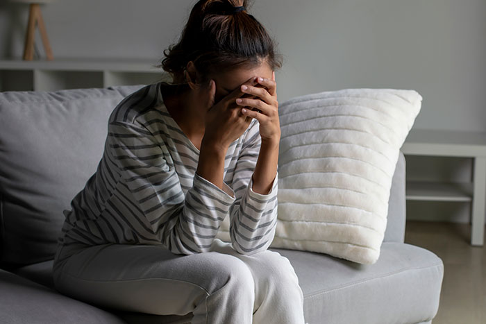 Woman sitting on a couch looking distressed and covering her face, reflecting on why she keeps getting sick. Woman sitting on a couch looking distressed and covering her face, reflecting on why she keeps getting sick.