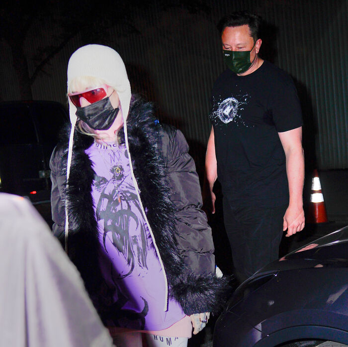 Grimes wearing a face mask and hat, showcasing a striking ringworm-inspired face tattoo while walking outdoors at night.