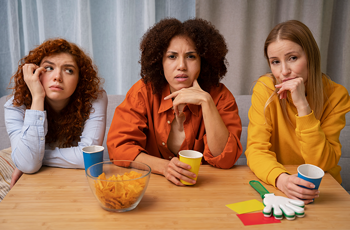 Three women sitting at a table looking concerned and thoughtful as sister reveals dead brother lie in a tense moment.