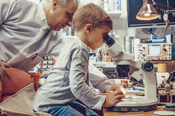 Young boy using a microscope with senior man watching, illustrating moments with famous family members discovering together.
