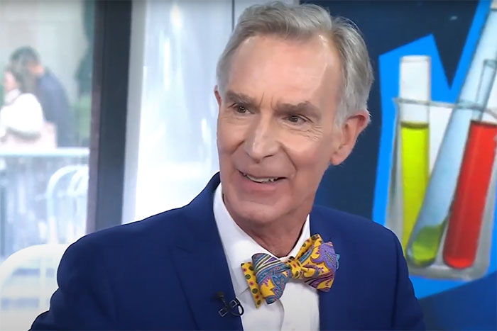 Man in a blue suit and colorful bow tie sharing moments about having famous family members on a TV show.