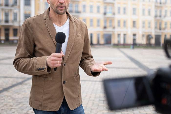 Man holding microphone reporting outdoors about people with famous family members sharing moments they found out and what it's like.