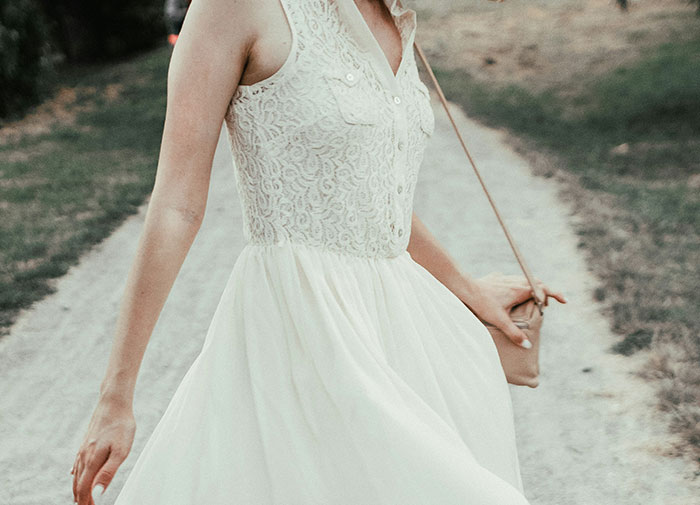 Woman walking outdoors wearing her own wedding dress with lace bodice and flowing skirt on a gravel path.