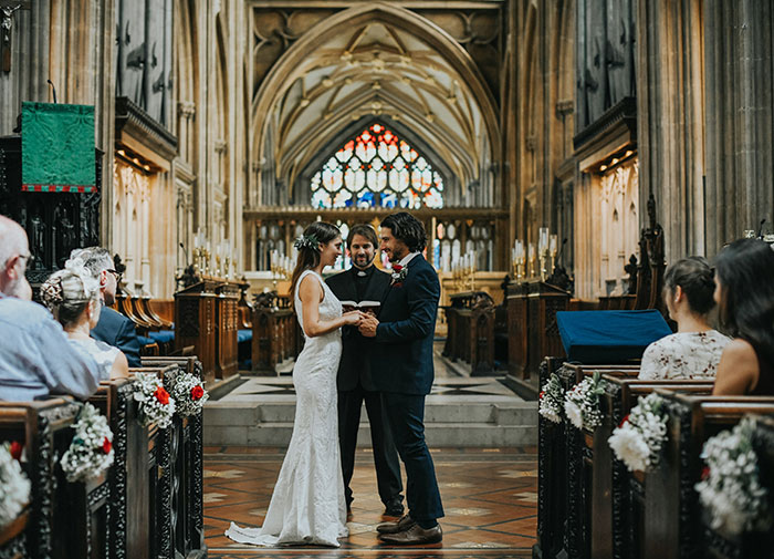 Bride in a wedding dress standing with groom at altar during ceremony with guests watching in church interior.