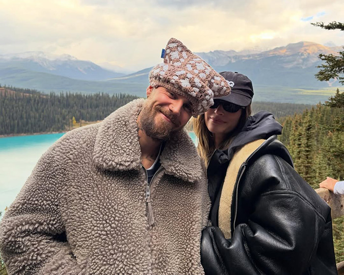 Hailey Bieber and friend wearing cozy winter coats with scenic mountain and lake view in the background.