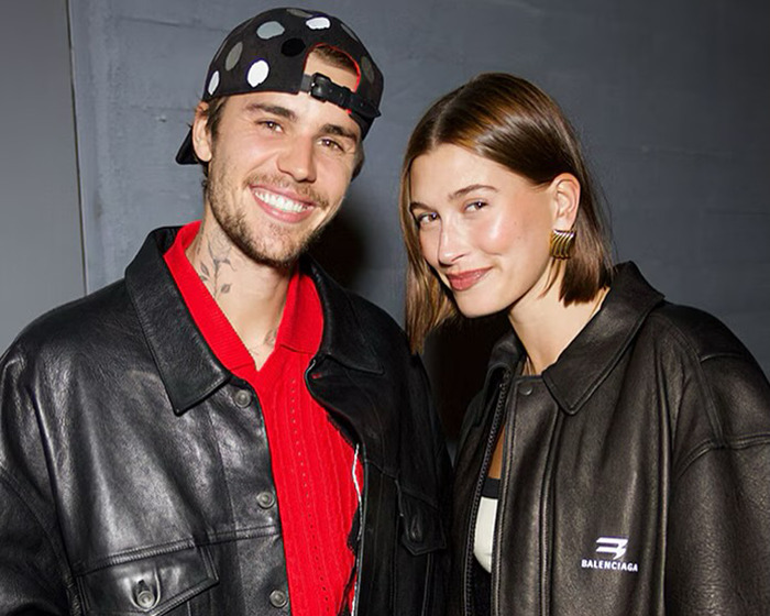 Hailey Bieber and Justin Bieber smiling together, both wearing black leather jackets in a casual setting.