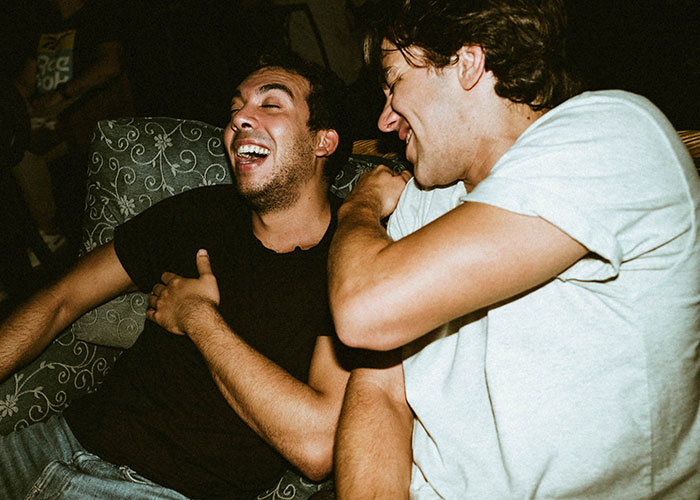 Two young men laughing together at a casual gathering, highlighting themes of masculinity and social discomfort.