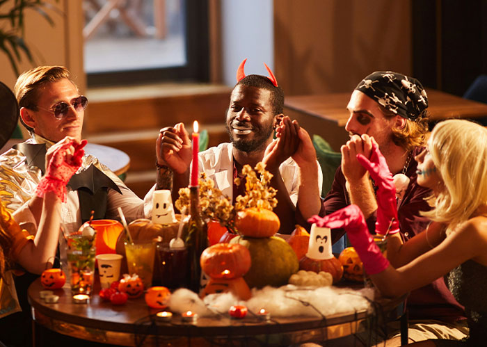 Group of friends in Halloween costumes celebrating at a decorated table, reflecting themes of a Halloween wedding event.