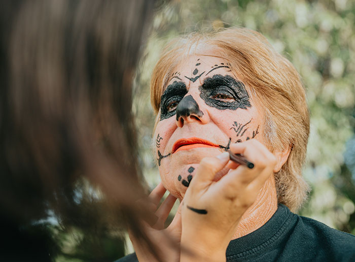Woman getting Halloween face paint applied outdoors, related to a Halloween wedding and guest reaction.