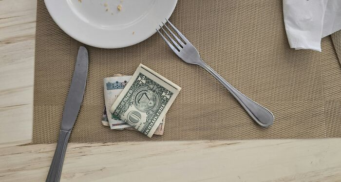 Folded dollar bills placed beside knife and fork on a restaurant table, illustrating stories when the bill comes but no payment.