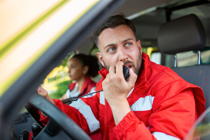 Emergency responder in red uniform speaking into a radio inside a vehicle during a strange 911 call situation.