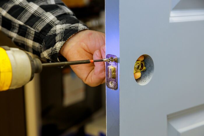 Close-up of a person using a drill to install a door lock, illustrating DIY challenges linked to drunk fumbles and bad decisions.