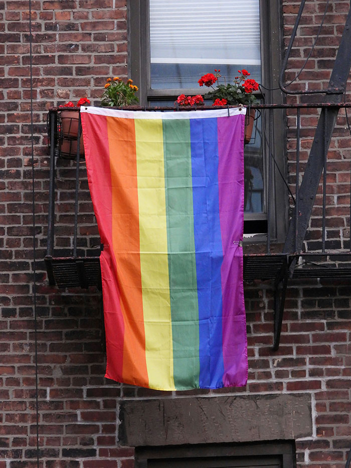 Rainbow pride flag hanging from a balcony with flowers against a brick wall, symbolizing LGBTQ+ support in Florida.