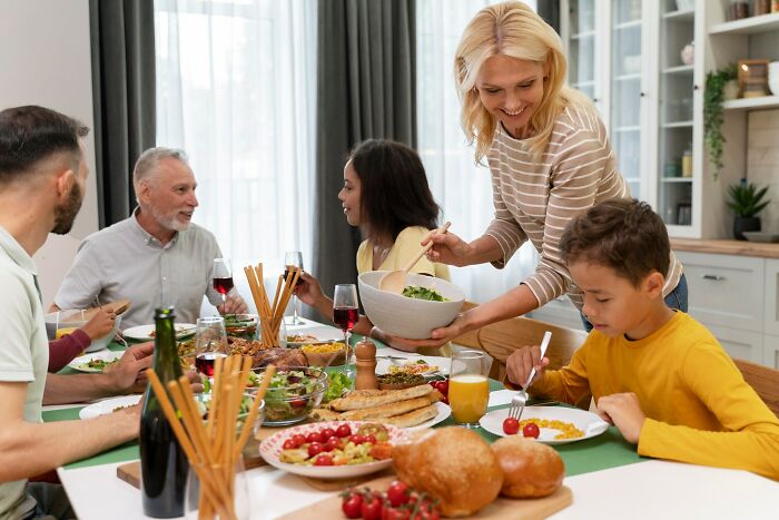 Family dinner scene with people socializing and serving food, capturing moments of misreading social cues humorously.