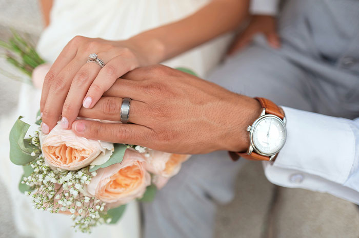 Close-up of a couple's hands with wedding rings over a bouquet, illustrating women sharing hardest truths about their lives.