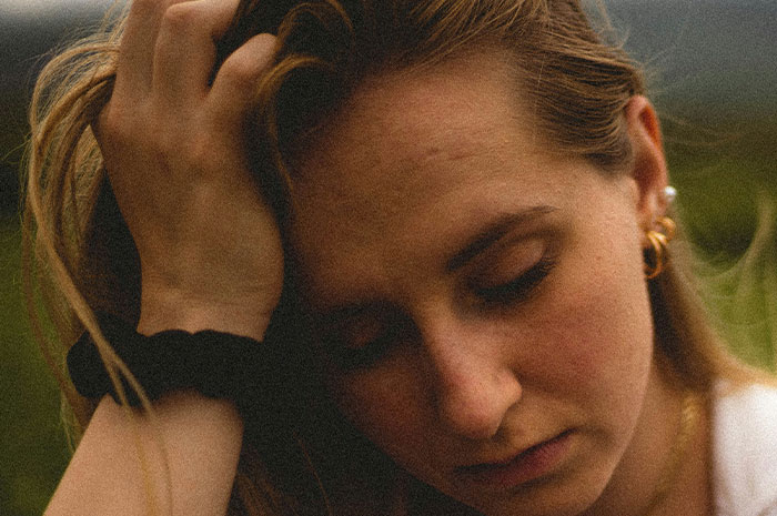 A woman with closed eyes and hand in hair reflecting on the hardest truths women had to accept in their lives.