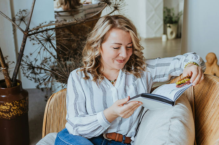Woman reading a book on a cozy couch, reflecting on the hardest truths women share about their lives.