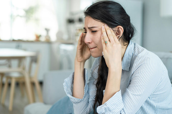 Stressed woman sitting indoors with eyes closed and hands on temples, reflecting on hardest truths in life.