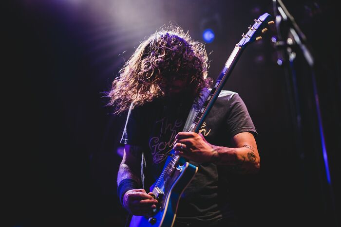 Man playing electric guitar on stage with dramatic lighting, embodying the essence of childhood rules and emotions.