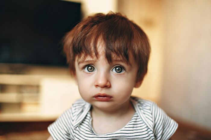 Toddler with wide eyes and messy hair looking concerned indoors, capturing the chaos of disastrous playdates parents remember.