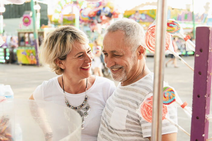 Smiling middle-aged couple enjoying a fair, taking advantage of fun and colorful carnival attractions together.