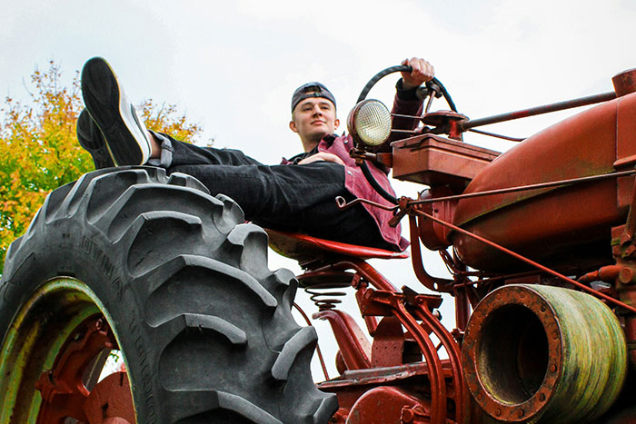 Young man relaxed on vintage tractor outdoors, representing a cool high school story about famous supermodels.