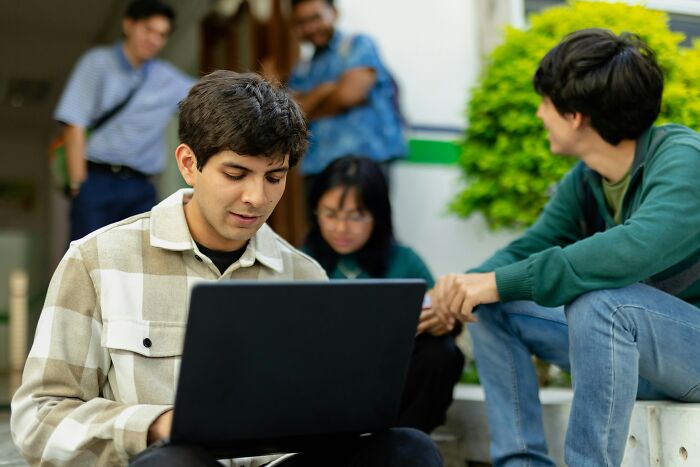 Group of young people gathered outdoors with one using a laptop, reflecting on stories about the most famous supermodel.