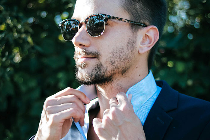 Man wearing sunglasses and a suit outdoors, adjusting his collar, representing the most famous supermodel style.