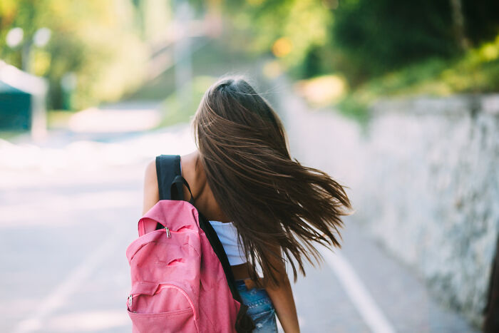 Young woman with long hair walking outdoors carrying a pink backpack, representing the most famous supermodel in the world.