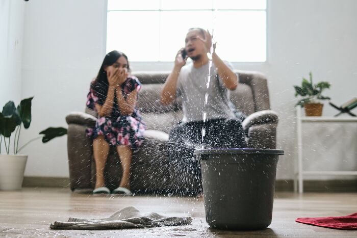 Couple reacting to a leaking bucket in living room, illustrating simple car stuff skills to handle unexpected problems.