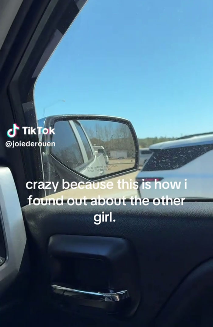 View from inside car showing side mirror with text about a woman finding out boyfriend is cheating in a weird way.