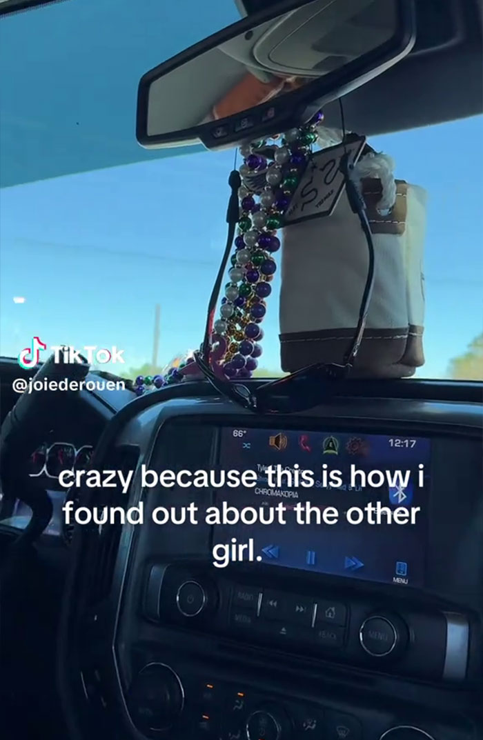 Interior of a car with a rearview mirror, sunglasses, and a dashboard showing a music player, relating to cheating story.