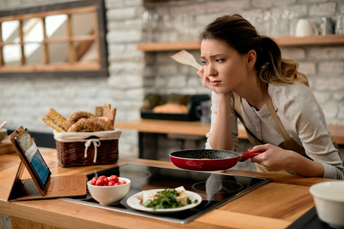 Mom looking frustrated in kitchen holding frying pan, facing hurdles to eat together with family, seeking connection.