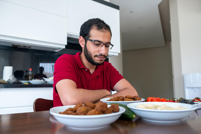 Man sitting alone at table with food looking down, depicting family mealtime hurdles and challenges to eat together.