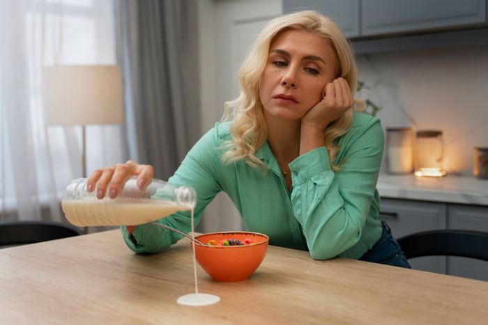 Mom looking discouraged while pouring milk on cereal alone, illustrating her struggle with eating together as a family.