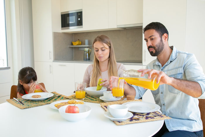Mom feeling frustrated while sitting with family struggling to eat together at the breakfast table in a modern kitchen.