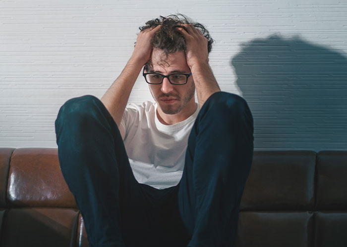 Man sitting on a couch with hands in hair, looking stressed and upset about lost savings for tummy tuck dreams.