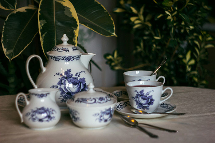Porcelain tea set with blue floral patterns displayed on a table amid green plants in a cozy setting.