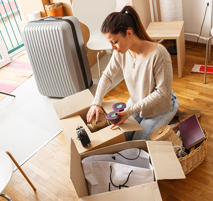 Woman packing tea set into a box near luggage, symbolizing conflict involving a stolen tea set and ruined marriage.