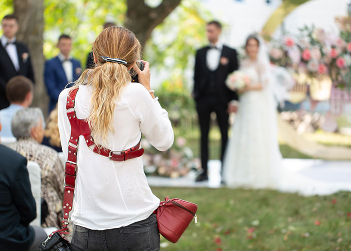 Woman wedding photographer taking pictures at outdoor ceremony, highlighting refusal to film coworker's wedding for free.