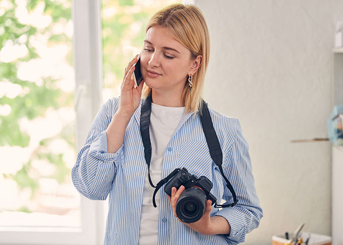 Woman photographer holding camera, talking on phone, possibly discussing a wedding filming request or refusal.