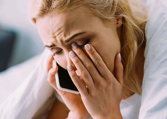 Woman upset on phone, refusing to film wedding for free, showing stress and frustration at home.