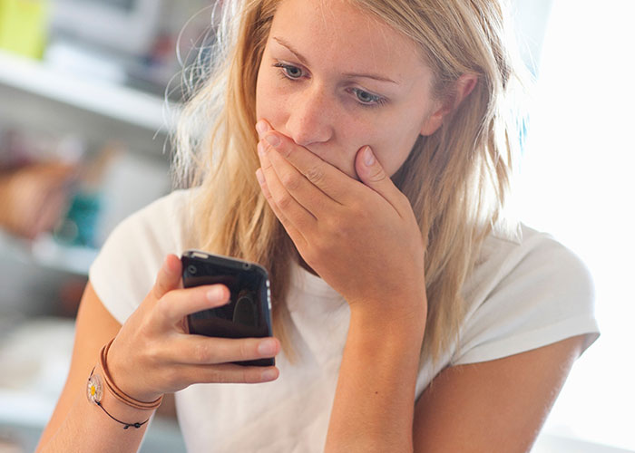 Woman looking shocked at phone, reacting to being dragged for refusing to film husband&rsquo;s coworker&rsquo;s wedding free