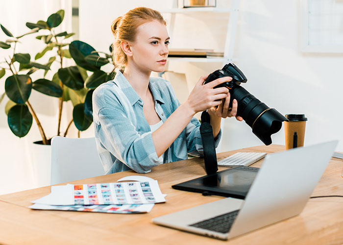 Woman photographer reviewing camera settings at desk, illustrating refusal to film coworker&rsquo;s wedding for free conflict.