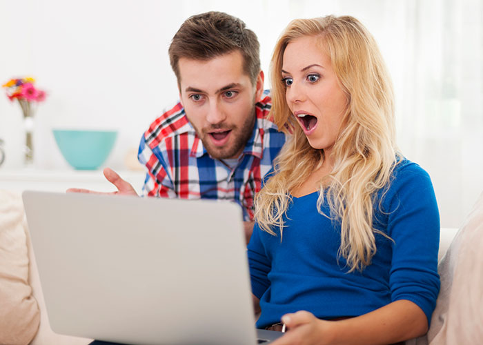 Couple looking shocked at laptop screen, reacting to woman refusing to film coworker&rsquo;s wedding for free.