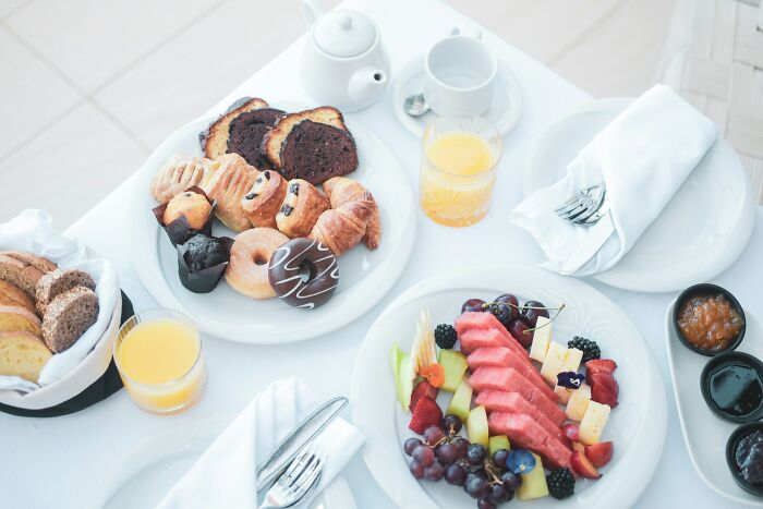 Assorted breakfast pastries and fresh fruit platter on a white table set for a casual meal.