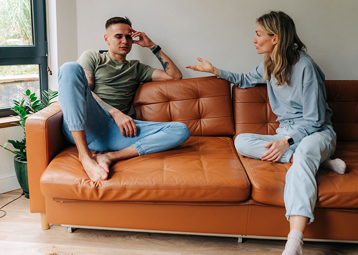 Young man and woman having a tense conversation on a couch representing men sharing icks that cause lost interest in women.