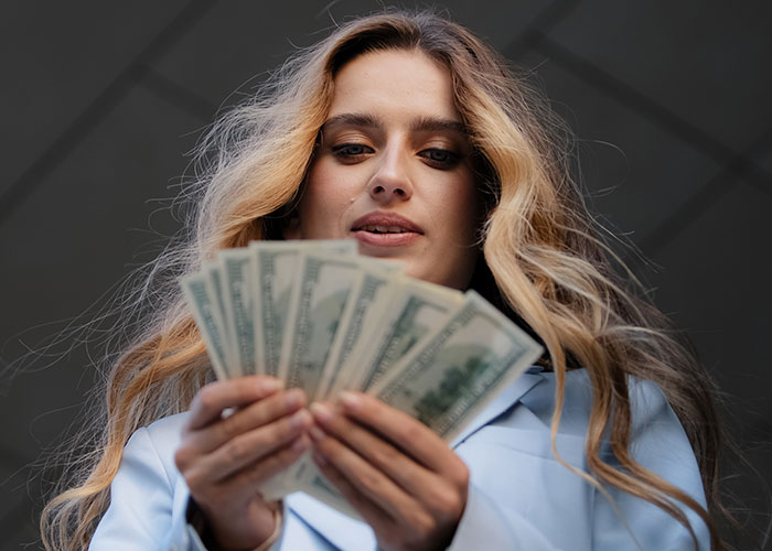 Young woman with long hair holding and counting dollar bills, illustrating icks men share that make them lose interest in a woman.