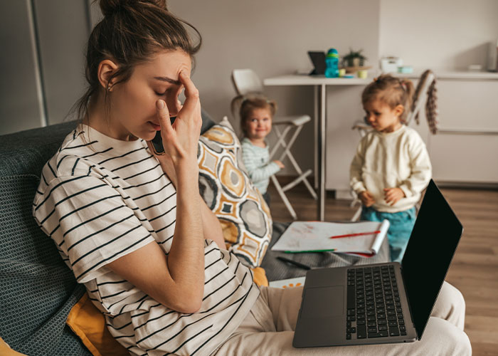 Stressed woman resting face in hand while children play in background, illustrating relationship icks men lose interest in.